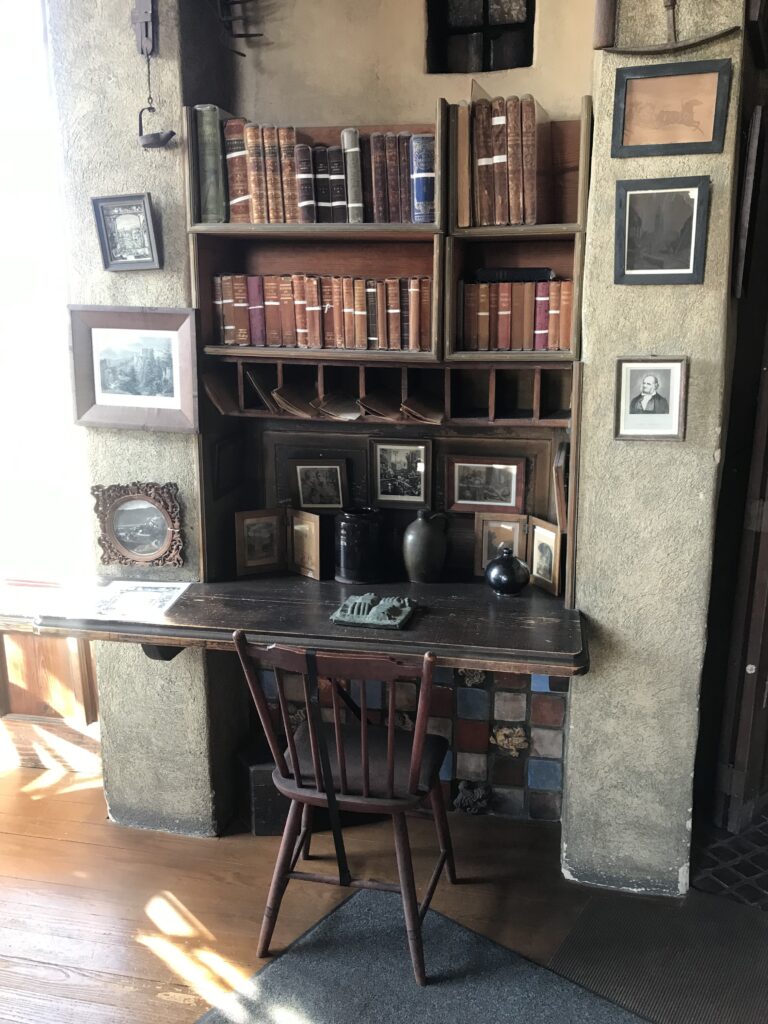 Vintage writing desk with wooden chair, bookshelves, and framed photos inside Fonthill Castle