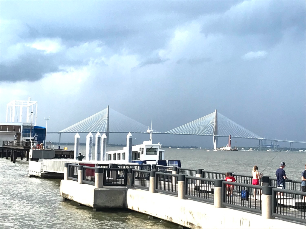 Waterfront pier with Arthur Ravenel Jr. Bridge in the background under cloudy skies