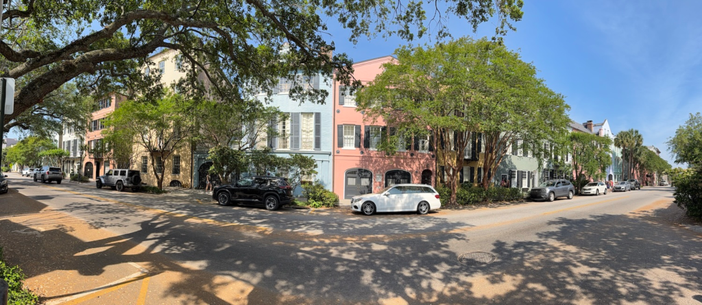 Colorful historic homes along Rainbow Row with oak trees and parked cars
