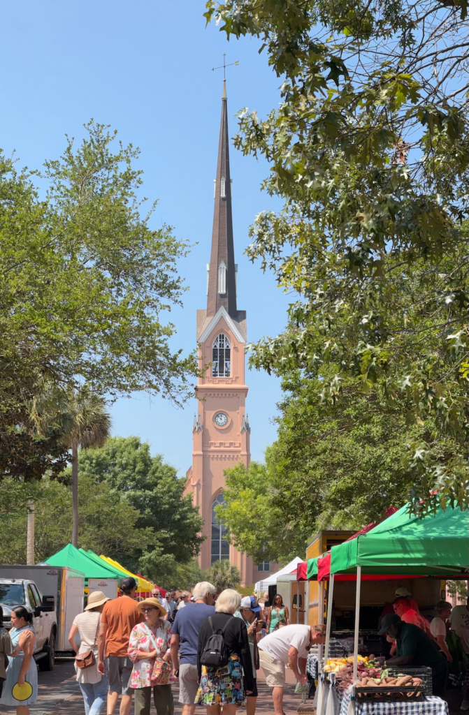 Charleston City Market with vendors and shoppers and St. Philip's Church steeple in the background