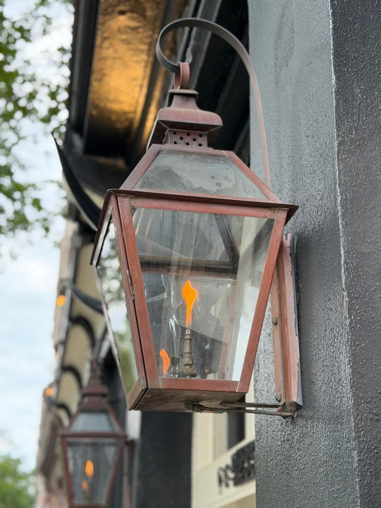 Historic gas lantern mounted on a building in Charleston, South Carolina with visible flame inside glass enclosure