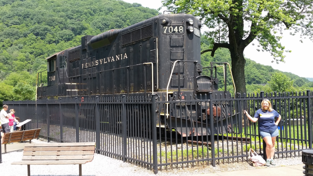 Historic Pennsylvania Railroad locomotive 7048 on display at Horseshoe Curve in Altoona, Pennsylvania with visitor standing by fence