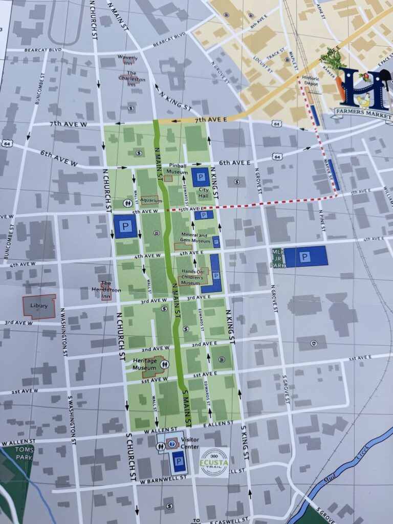 A visitor map of downtown Hendersonville, North Carolina, showing Main Street, parking areas, museums, the visitor center, and popular attractions within the walkable historic district.