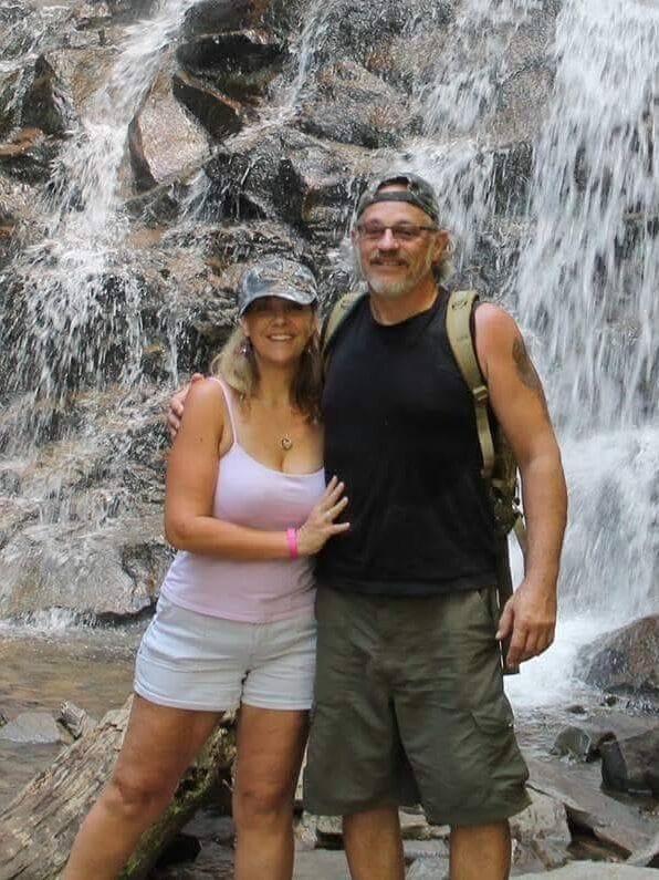A couple standing together in front of a rocky waterfall during a scenic outdoor hike, enjoying a day exploring nature.