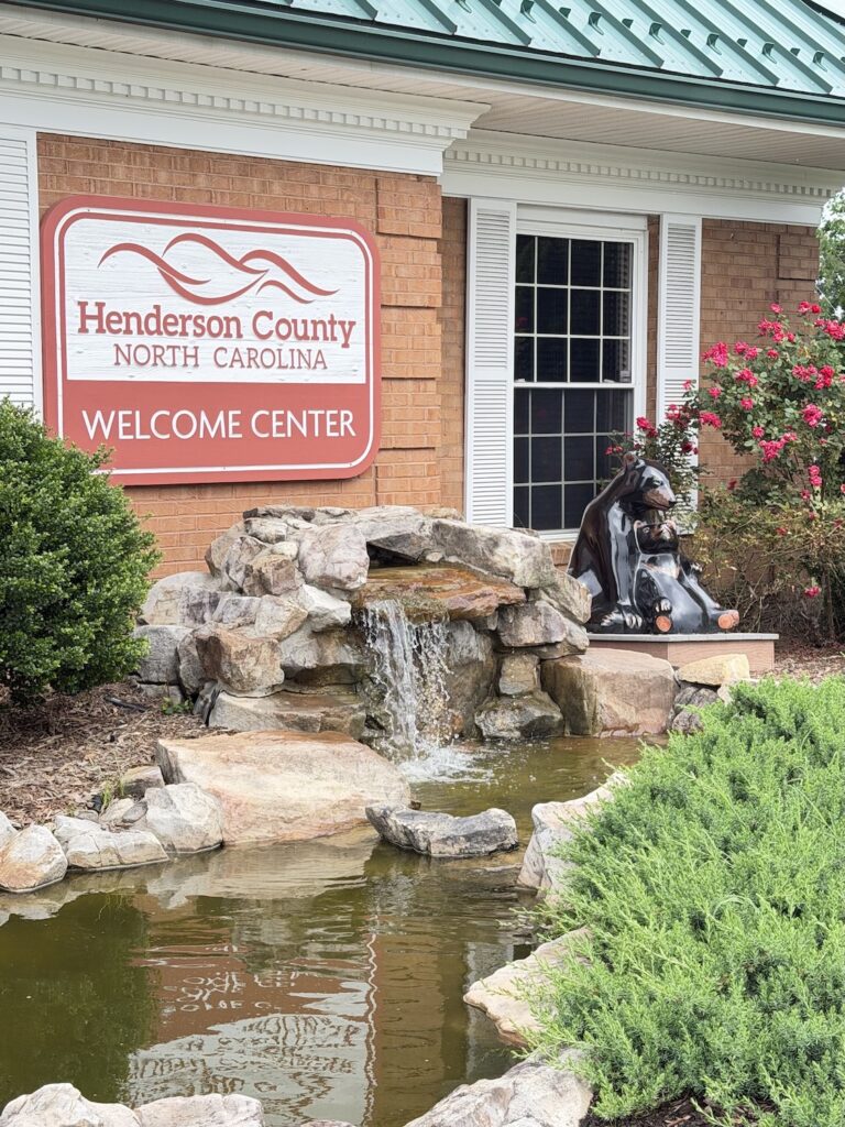 Henderson County Welcome Center in Hendersonville, North Carolina, featuring a decorative waterfall, landscaped garden, and a bear sculpture near the entrance.