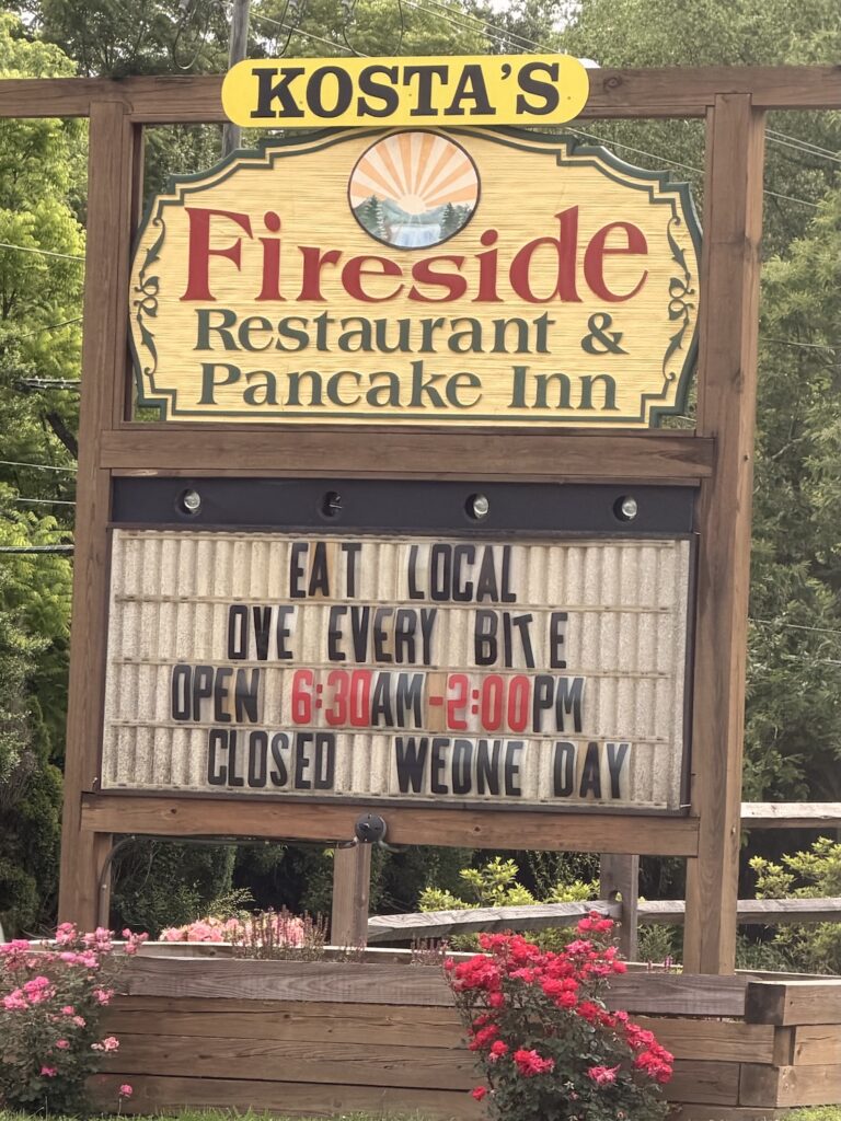 Roadside sign for Kosta's Fireside Restaurant & Pancake Inn in Hendersonville, North Carolina, displaying business hours and promoting local dining.