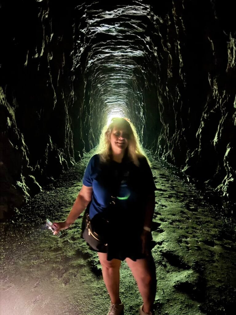 Visitor standing inside Stumphouse Tunnel with sunlight glowing from the tunnel opening behind her.
