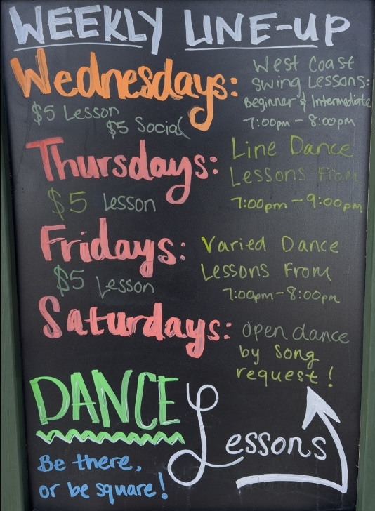 Weekly dance lesson schedule board at Honeysuckle Holler showing line dancing and West Coast Swing classes.