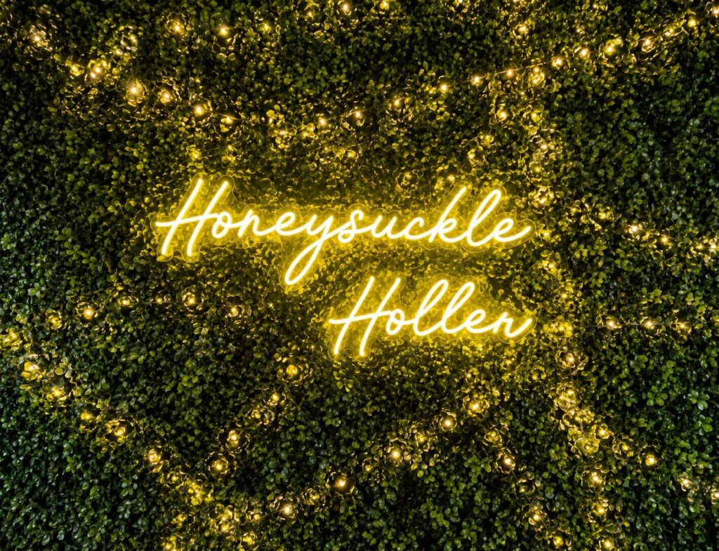 Illuminated Honeysuckle Holler neon sign displayed on a decorative greenery wall inside the Hendersonville, North Carolina dance venue.