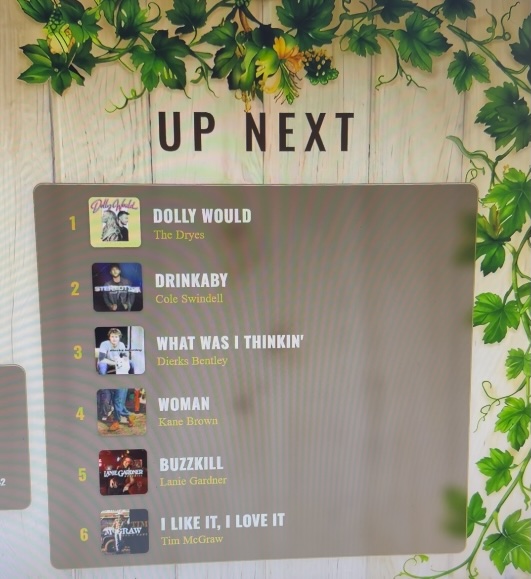 Digital song queue display at Honeysuckle Holler showing upcoming country songs for line dancing in Hendersonville, North Carolina.